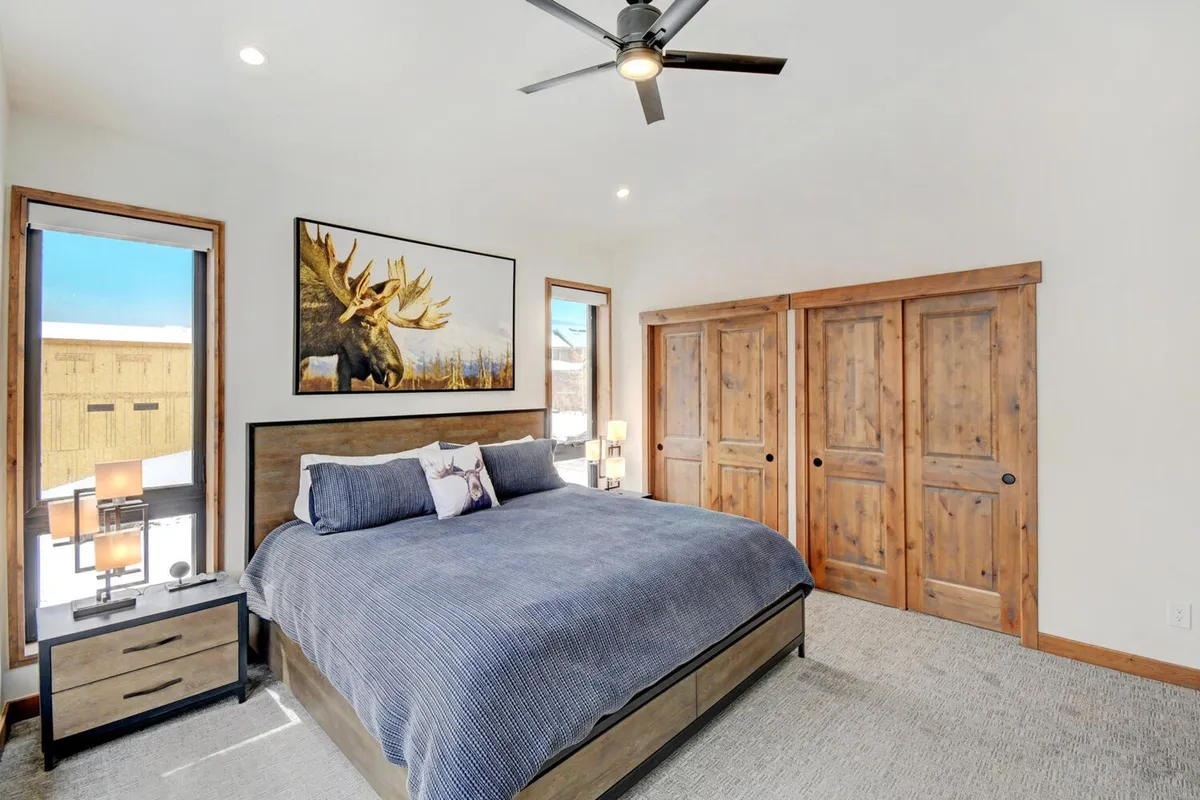 A serene, king-sized bedroom featuring a plush bed with premium bedding, moose artwork, and inviting wooden closet doors. Natural light filters in, creating a cozy atmosphere perfect for restful nights.