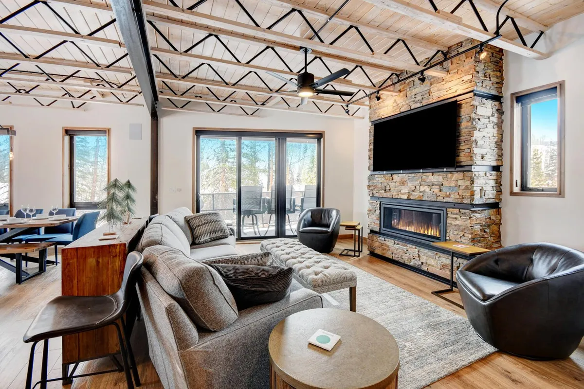 An elegant living area with a stone fireplace, modern sofas, large windows offering views of the surrounding landscape, and warm wooden accents. The scene is set for both intimate gatherings and relaxed, scenic enjoyment.