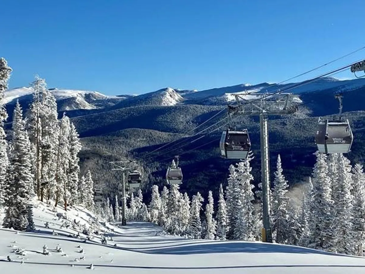 A panoramic view of the ski lift gliding above snow-covered trees and a mountain range beneath a clear blue sky. The scene captures the thrill of winter sports and the tranquil beauty of the alpine setting, suggesting a wide range of winter adventures available nearby.