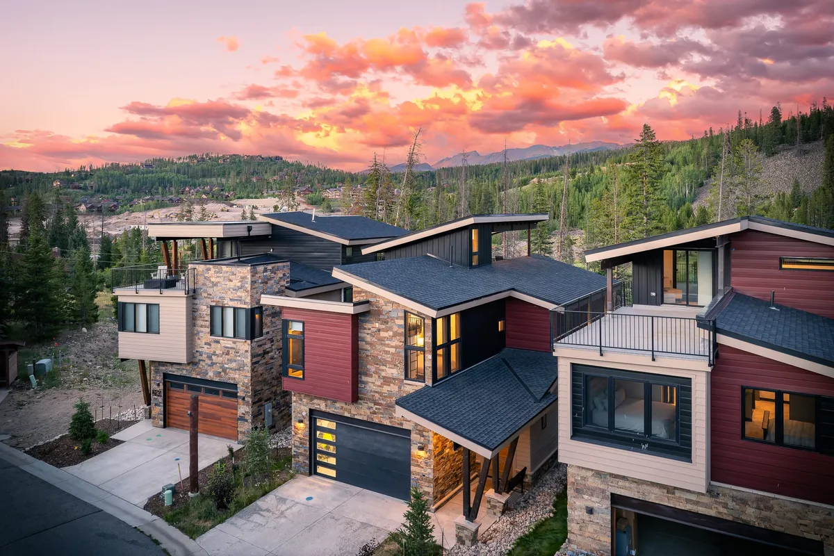 An exterior view of the property’s modern architecture, stone facade, and vibrant sunset-lit sky. The image conveys the home’s elevated position and the promise of spectacular views from the rooftop deck.
